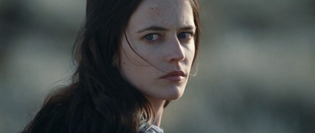 Actriz Eva Green con cabello oscuro mojado, expresión seria y mirada penetrante, sobre fondo desenfocado grisáceo
