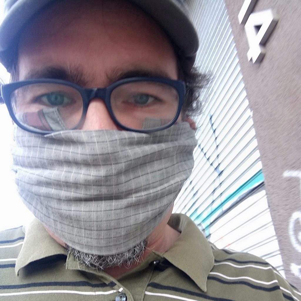 Rodrigo Zúñiga con gafas y mascarilla gris a cuadros, mirando hacia la cámara en interiores