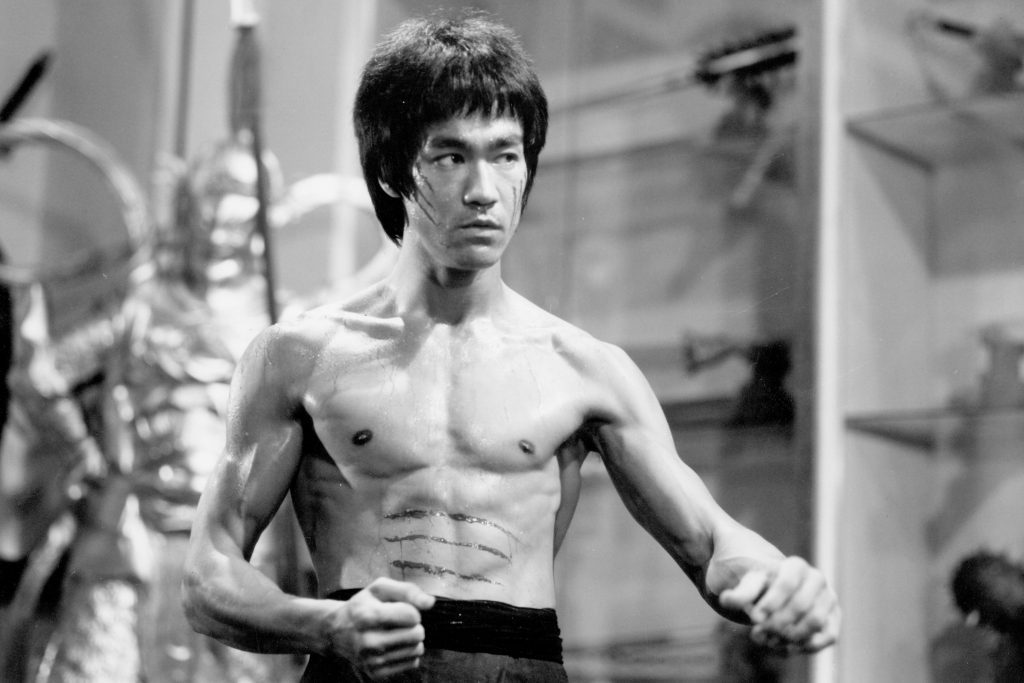Bruce Lee sin camisa en postura de combate, mostrando su musculatura definida en blanco y negro