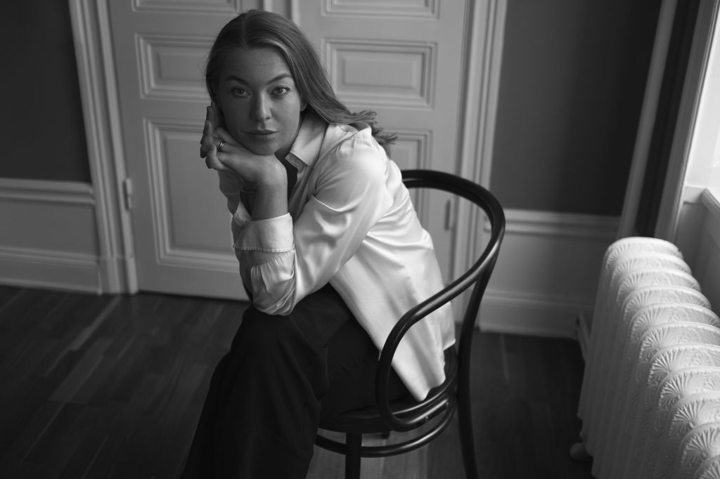 Karolina Ramqvist, autora sueca, posada en silla de madera en interiores minimalistas, fotografía en blanco y negro