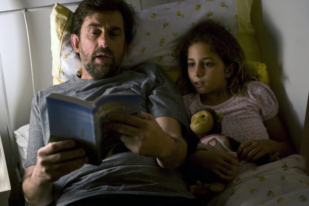 Hombre adulto y niña pequeña en cama leyendo juntos un libro azul, ambiente íntimo y doméstico