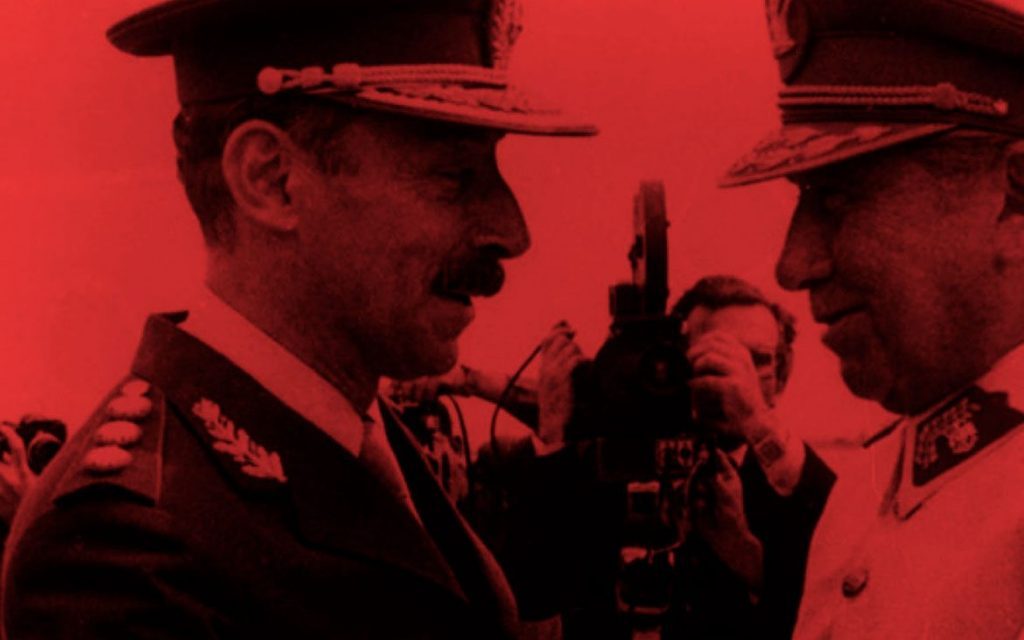 Dos oficiales militares en uniforme con sombreros ante fondo rojo intenso, escena de drama político sudamericano