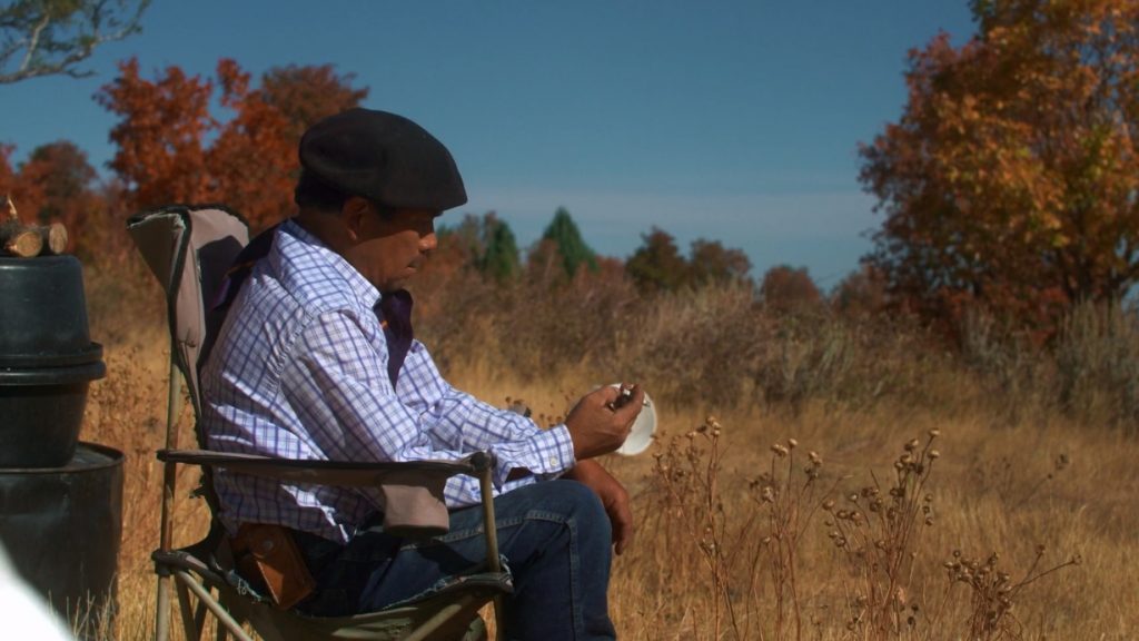 Hombre sentado en silla de ruedas leyendo en paisaje rural otoñal con árboles secos y cielo despejado
