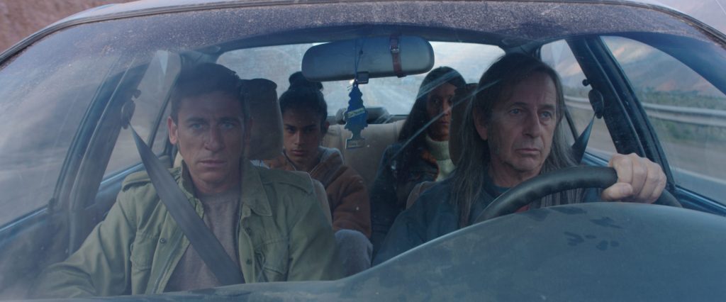 Grupo de personas dentro de un automóvil visto a través del parabrisas, en escena de tensión durante viaje nocturno