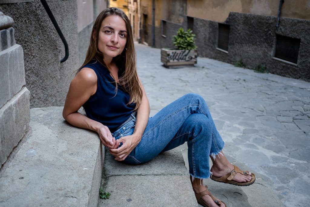 Irene Solá, autora de Canto yo y la montaña baila, sentada en una calle de piedra con jeans y top azul