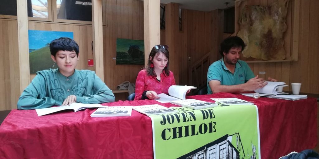 Tres personas en mesa de panel con micrófono, cartel visible con nombre Juan Pablo Mosqueira, ambiente de evento