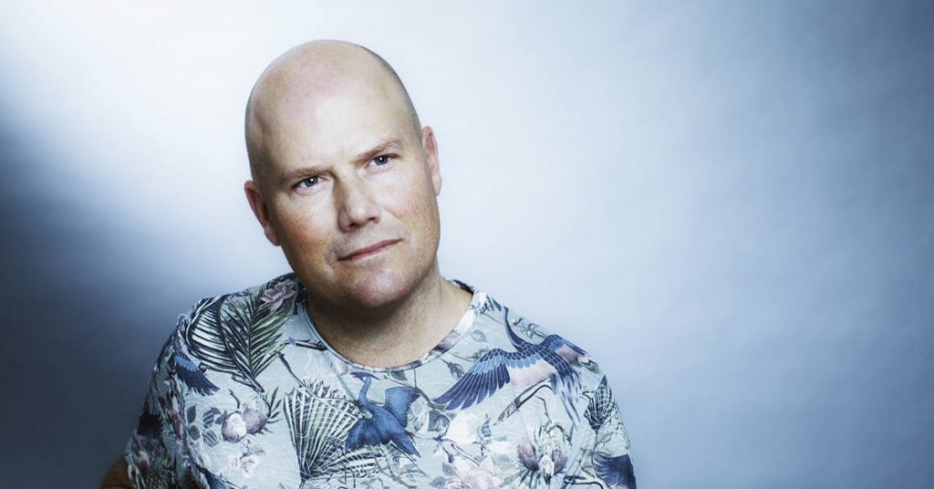Mattias Edvardsson, autor sueco, retrato de estudio con fondo azul y camiseta de patrón geométrico