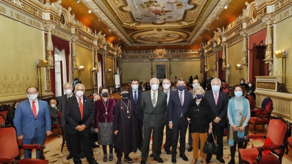 Grupo de hombres y mujeres en traje formal posando en salón ornamentado con decoración dorada y techos artesanales