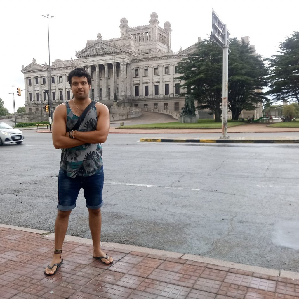 Williams Arévalo posa frente a un edificio de arquitectura neoclásica en una plaza urbana lluvia