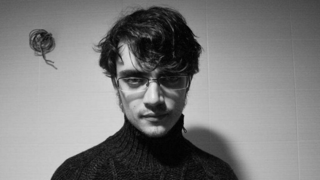 Hombre joven con gafas oscuras y suéter negro en fotografía en blanco y negro de perfil frontal