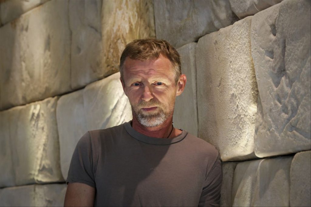 Jo Nesbø, escritor noruego, retratado contra una pared de piedra en tonos grises y beige