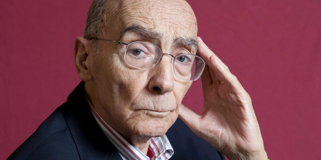 Retrato del escritor portugués José Saramago con gafas, fondo granate, mano en la mejilla en expresión pensativa