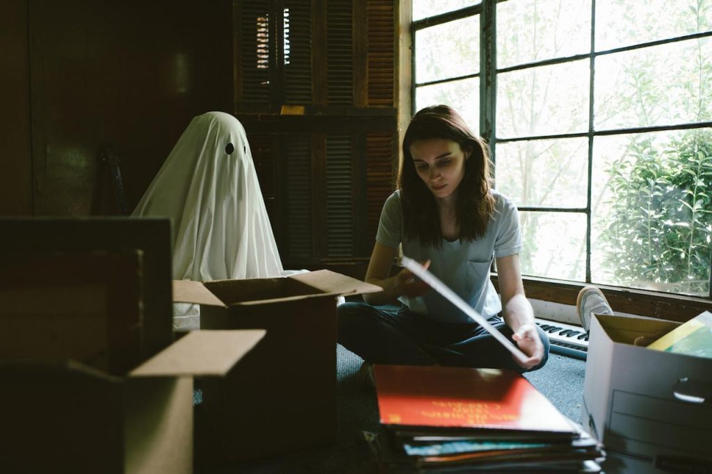 Mujer joven frente a una máquina de escribir en habitación con ventana grande, sosteniendo papel blanco, ambiente