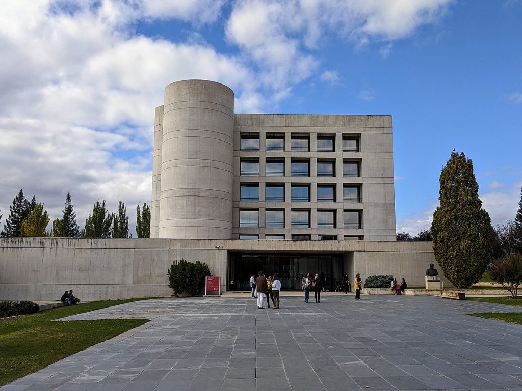Fachada de la Biblioteca de la Universidad de Navarra con torre cilíndrica de hormigón y plaza frontal
