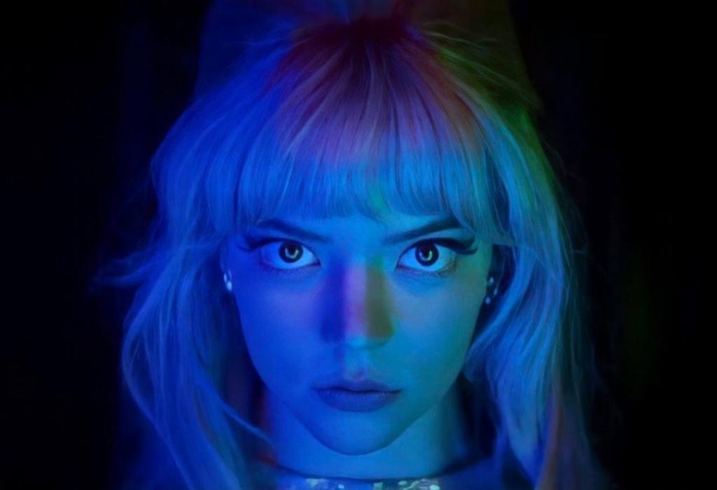 Mujer con cabello rubio platinado y flequillo, iluminada con luz azul neón, expresión seria mirando a cámara