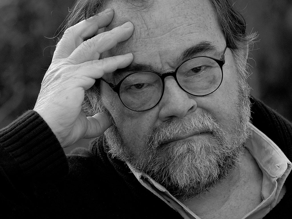 Retrato en blanco y negro de Luis Poirot, fotógrafo y documentalista chileno, con gafas redondas y barba, mano