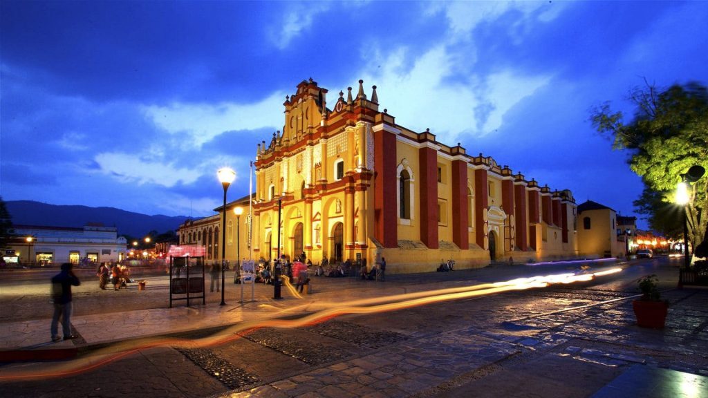 Iglesia colonial iluminada al atardecer en San Cristóbal de Las Casas, con plaza empedrada y personas caminando