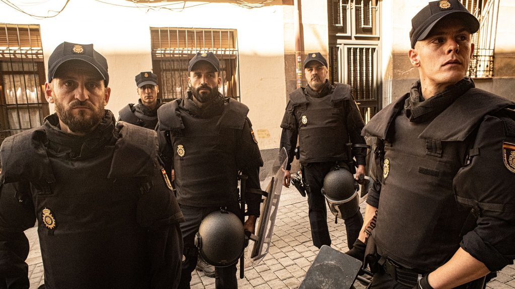 Agentes de policía antidisturbios en uniforme táctico patrullando una calle de adoquines en ambiente urbano