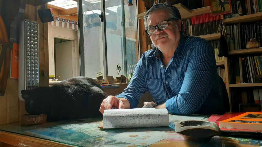David Avello, escritor, sentado ante su escritorio con máquina de escribir en su estudio lleno de libros