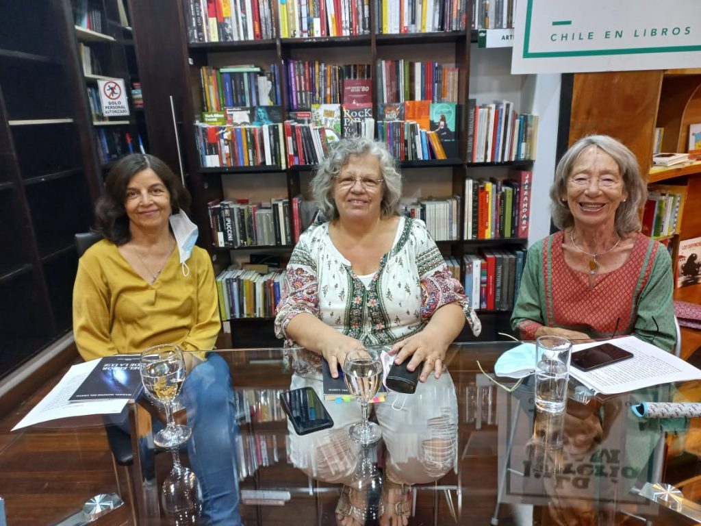 Tres mujeres en biblioteca sonríen ante la cámara. Marisol Moreno del Canto en el centro, junto a estanterías de libros