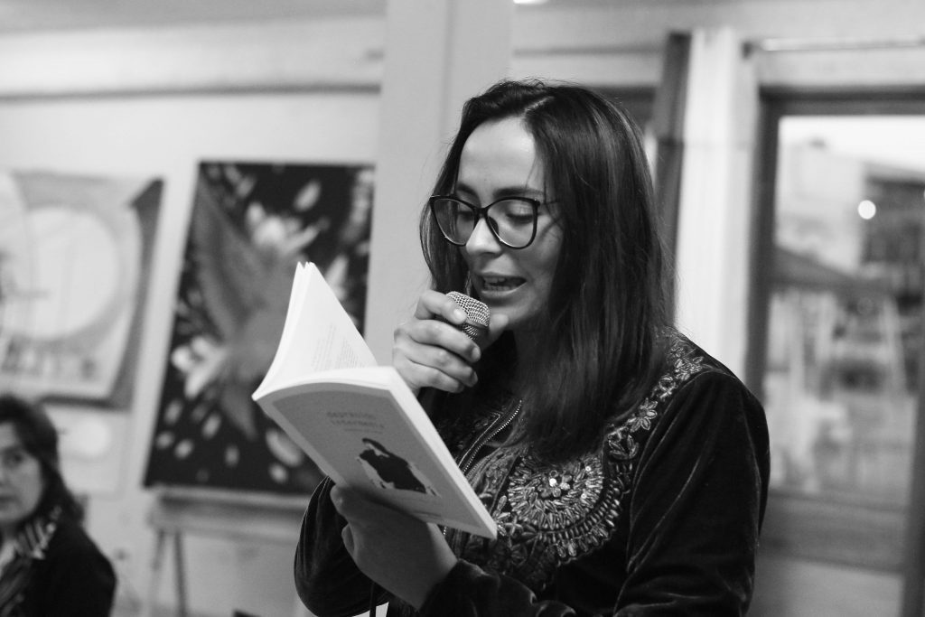 Mujer con gafas leyendo un documento en evento cultural, ambiente de galería o sala de exposiciones