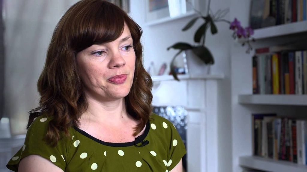 Bethany Roberts sonriendo, viste blusa verde con lunares blancos, fondo de estantería con libros