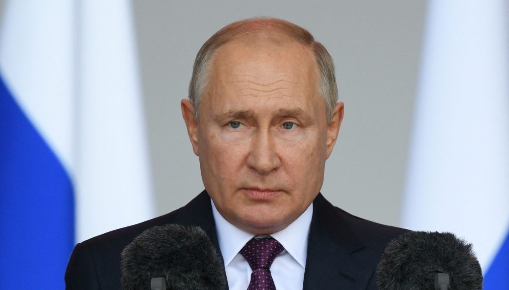 Vladimir Putin en conferencia de prensa, de traje oscuro y corbata, frente a fondo con bandera rusa