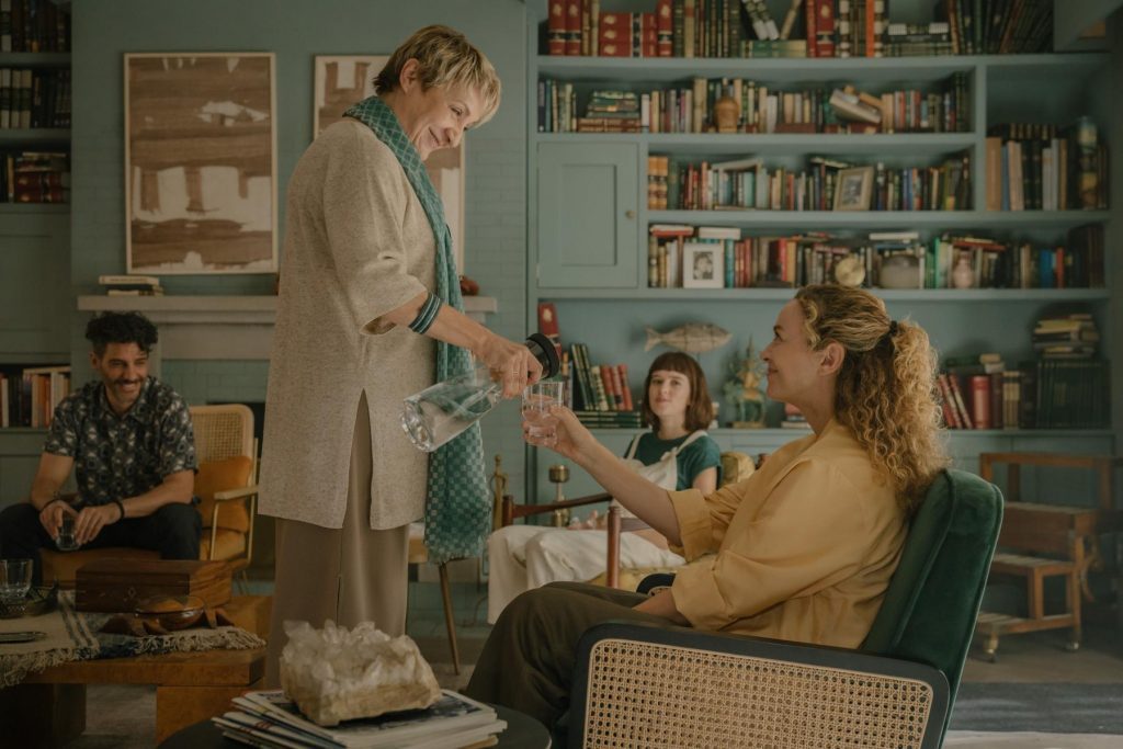 Hombre de traje beige de pie conversando con mujer en sala de estar decorada con libros y plantas verdes