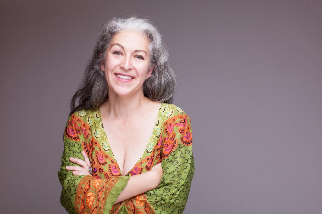 Joanna Mora, ilustradora, sonríe ante la cámara vistiendo blusa estampada en tonos verdes y naranjas