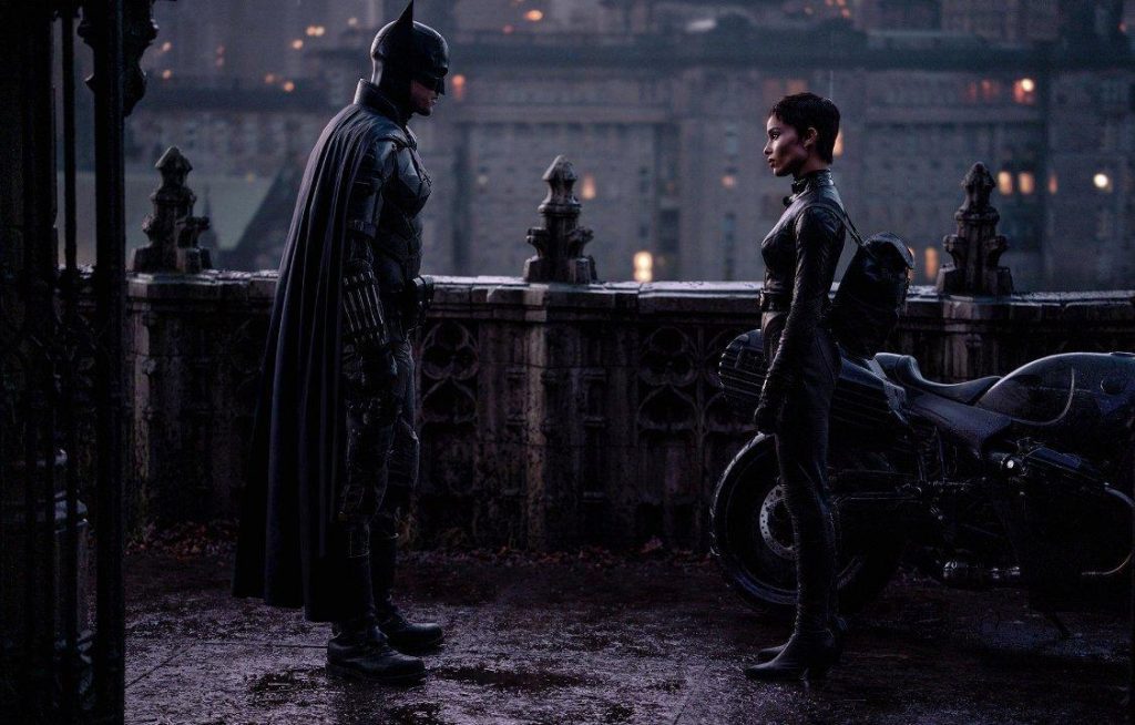 Dos figuras en la lluvia nocturna de Gotham, una de ellas vistiendo el traje oscuro del Murciélago, frente