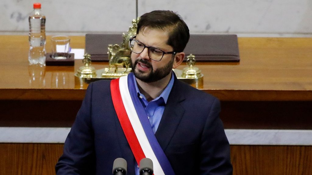 Gabriel Boric con banda presidencial tricolor, gafas, barba, en acto oficial
