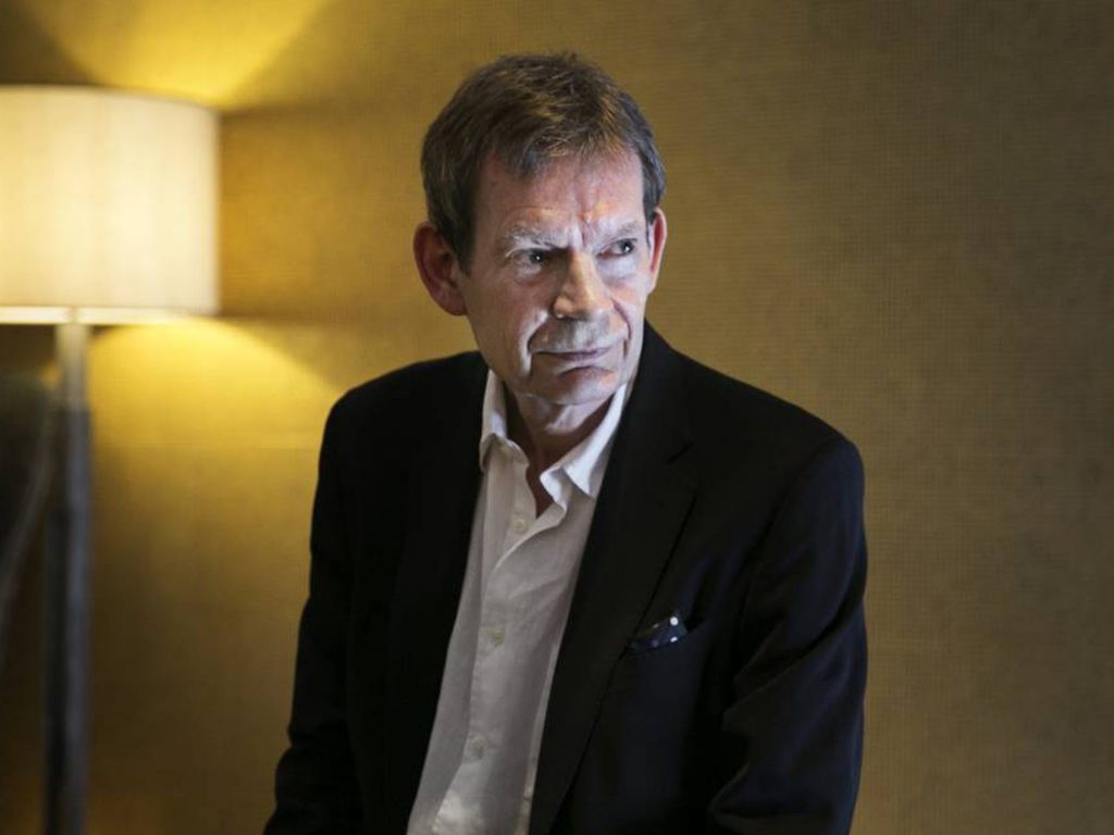 Graham Swift, escritor británico, retratado en interior con iluminación cálida, vistiendo blazer oscuro sobre camisa
