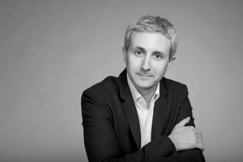 Retrato en blanco y negro de Ivan Jablonka, historiador francés, con blazer negro y camisa blanca sobre fondo gris