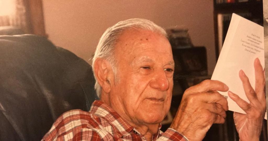 Escritor Carlos Droguett sostiene papeles mientras sonríe en interiror, retrato fotográfico de época