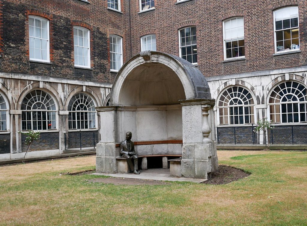 Monumento a John Keats en patio de edificio histórico de ladrillo rojo con arcos y ventanas clásicas