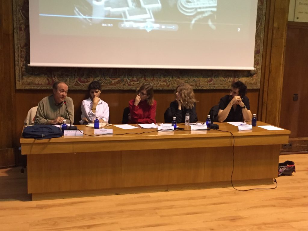 Panel de cinco personas sentadas en mesa de madera ante proyector en auditorio, durante presentación o debate sobre cine