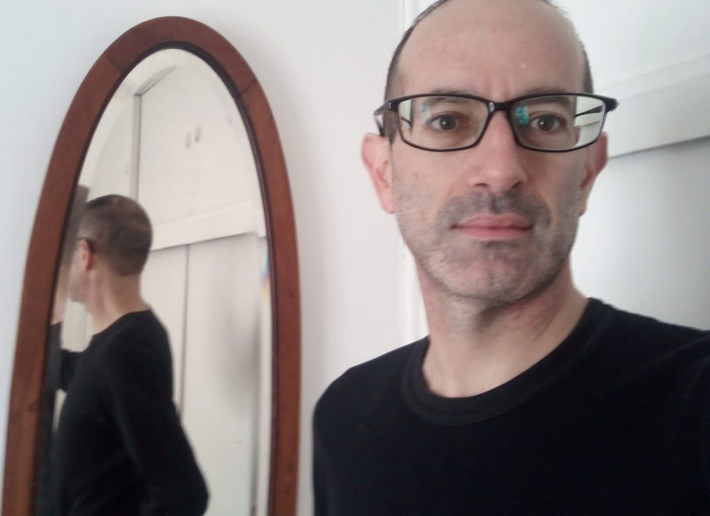 Nicolás Poblete frente a un espejo ovalado de marco marrón, con reflejo de su figura de fondo