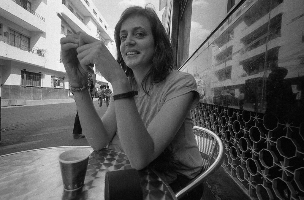 Mujer sostiene cigarrillo frente a edificios de apartamentos en blanco y negro, escena de tensión urbana