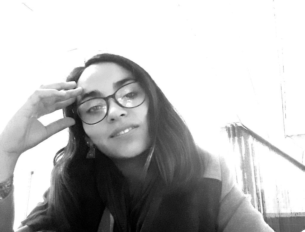 Mujer de cabello largo y lentes redondos ajustándose las gafas, fotografía en blanco y negro