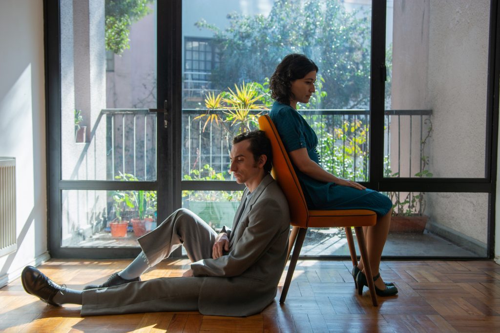 Dos personas practican yoga en un departamento moderno con vista a la ciudad, realizando posiciones de equilibrio