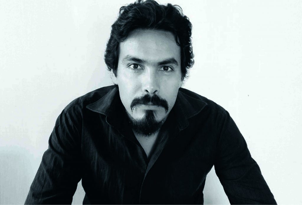 Retrato en blanco y negro de hombre de mediana edad con barba oscura y cabello negro, vistiendo camisa negra