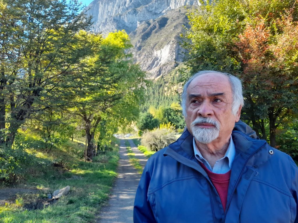Juan Mihovilovich en sendero boscoso con montaña de fondo, vistiendo chaqueta azul
