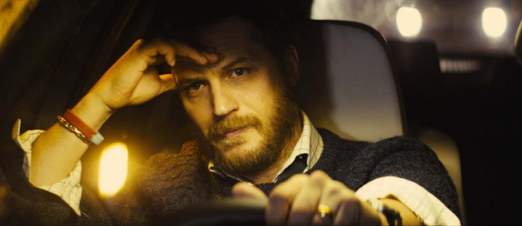 Hombre dentro de un automóvil en primer plano, tocándose la cabeza con la mano, con luces ambientales al fondo