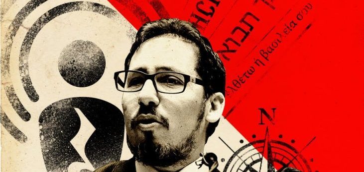 Víctor Ilich, hombre con gafas y barba, sosteniendo una cámara de cine frente a fondo rojo con elementos gráficos