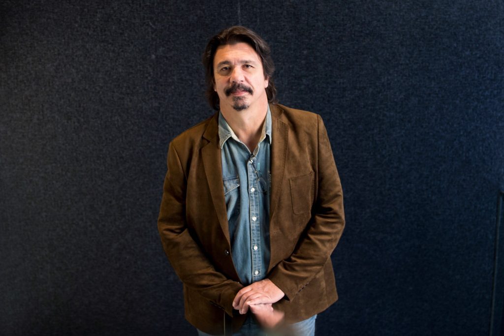 Dardo Scavino, hombre de mediana edad con bigote, chaqueta marrón y camisa azul, mirando hacia arriba contra fondo