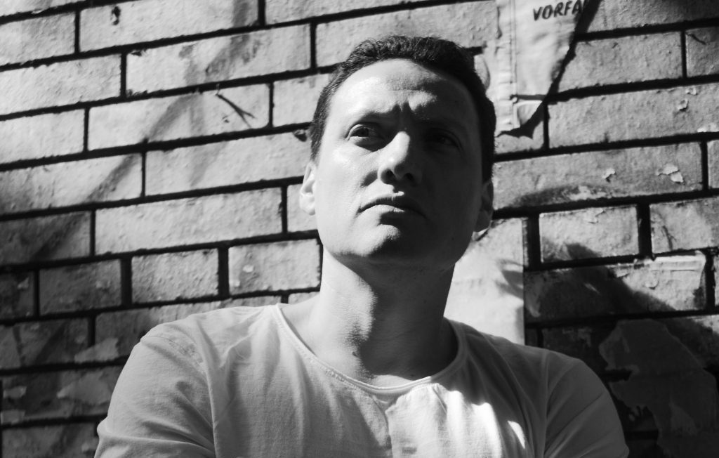 Retrato en blanco y negro de Esteban Catalán apoyado contra pared de ladrillos, mirando hacia un lado