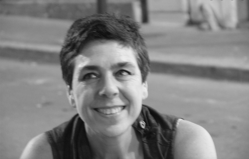 Retrato en blanco y negro de Pola Iriarte, sonriente, en primer plano de una calle urbana