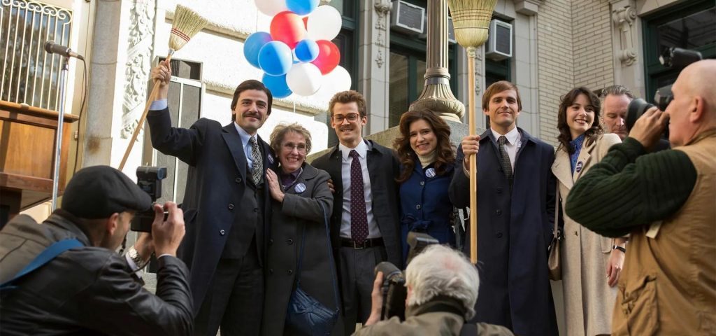 Grupo de personas en traje formal celebrando frente a un edificio, con globos rojos, blancos y azules de fondo
