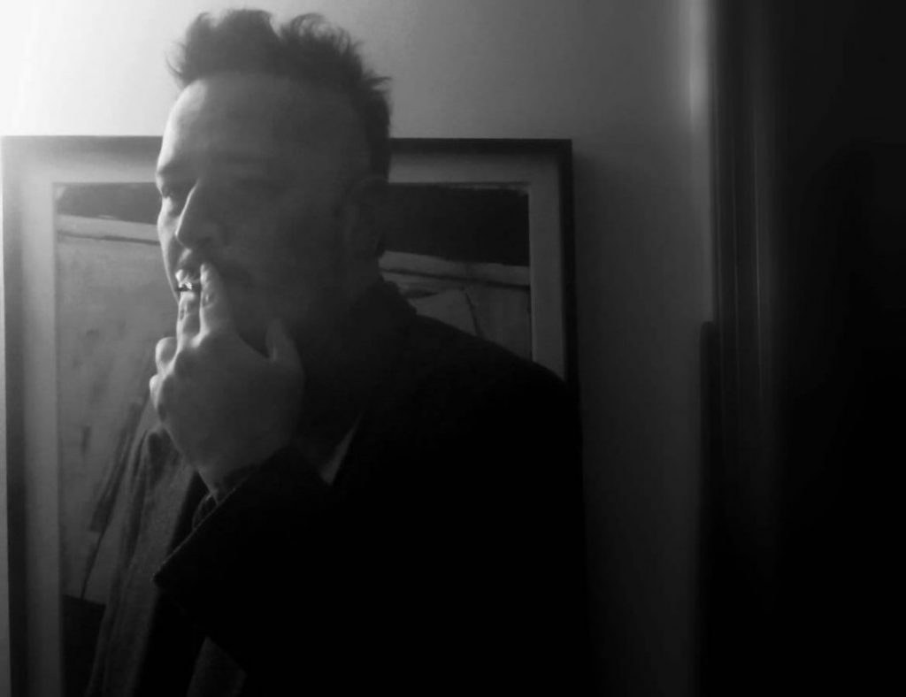 Retrato en blanco y negro del poeta Fabián Burgos, de perfil, en ambiente interior con luz dramática