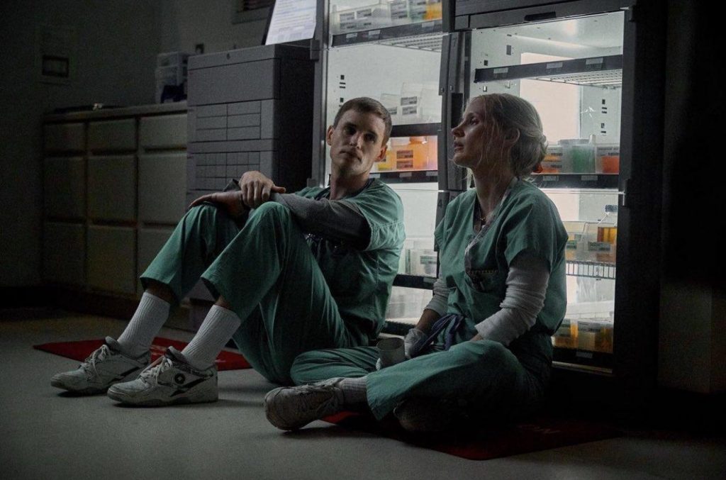Dos jóvenes en uniforme verde sentados en el piso frente a un refrigerador iluminado en ambiente oscuro